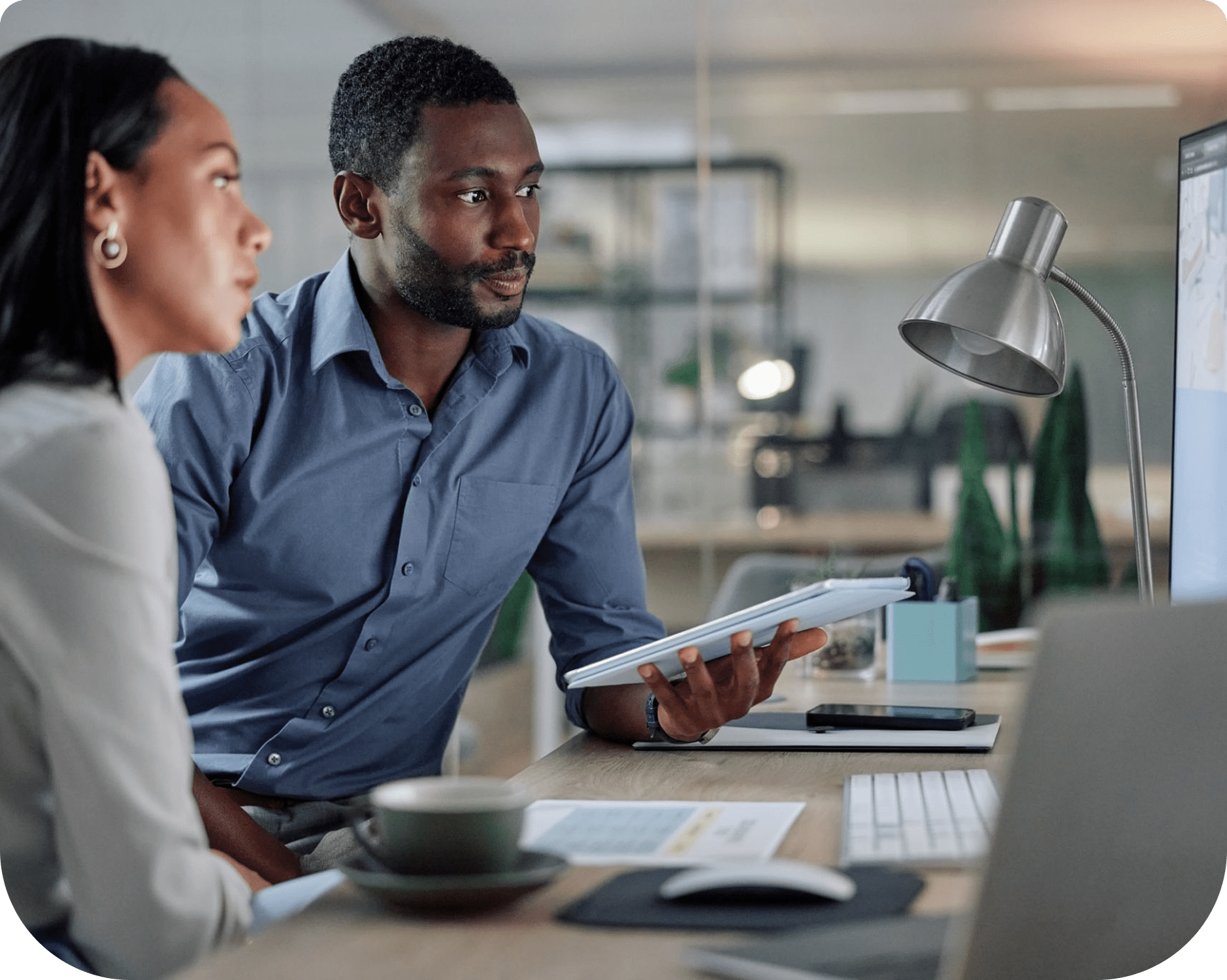 Two colleagues discussing work at desk.